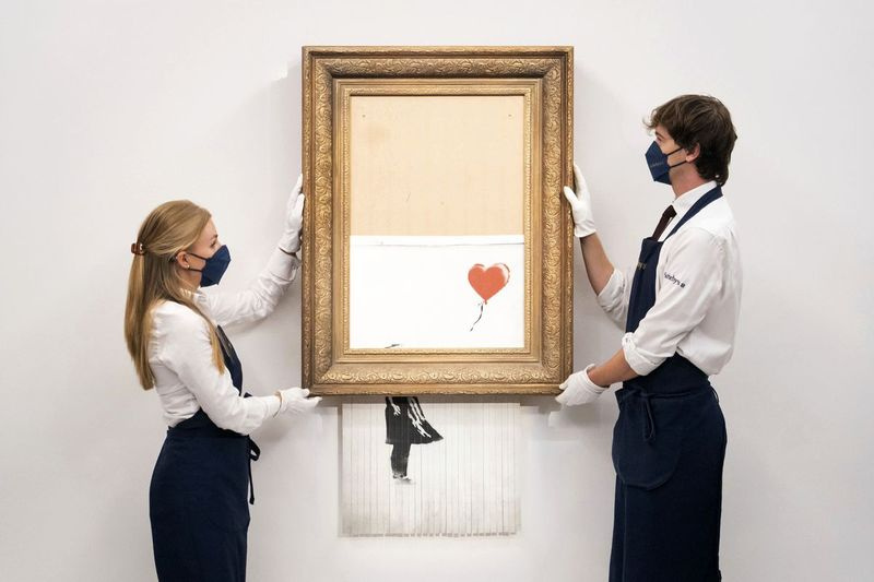 Auf diesem Dateifoto vom 3. September 2021 halten Kunsthändler des Auktionshauses Sotheby’s Banksy’s Love is in the Bin, nachdem es nach dem Verkauf auf einer Auktion auf mysteriöse Weise zerfetzt wurde.