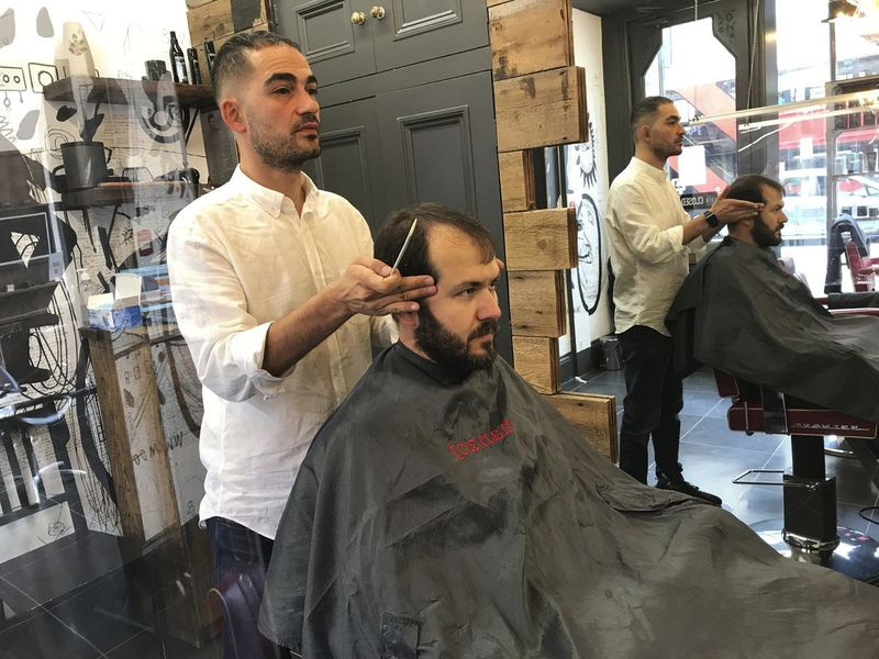 Rado Asatrian tunde părul unui client la salonul de coafură Man-oj din districtul financiar din Londra. Înainte de COVID-19, Asatrian avea de obicei 10 până la 15 clienți pe zi, dar acum a scăzut la trei sau patru.