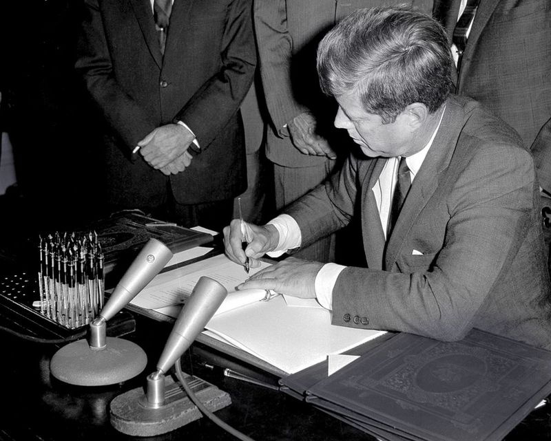 Nesta foto de arquivo de 7 de outubro de 1963, o presidente John F. Kennedy assina o Tratado de Proibição de Testes Limitados durante uma cerimônia de ratificação na Sala de Tratados da Casa Branca em Washington. | Foto / arquivo AP