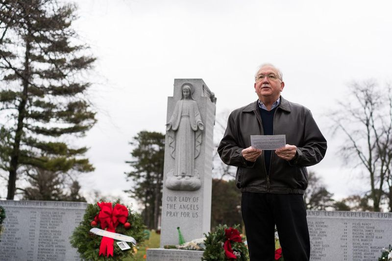 Serge Uccetta, ein Überlebender des Brandes der Our Lady of Angels School im Jahr 1958, leitet eine Zeremonie auf dem Queen of Heaven Cemetery, um an die Menschen zu erinnern, die an diesem Tag ihr Leben verloren haben. Hinter ihm ist ein Schrein, in dem viele der Opfer begraben sind.