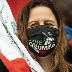 Madia Crudele, 46 ans, de Harwood Heights, porte un masque Save Columbus Day et agite un drapeau italien pendant le Columbus Day: Italian American Heritage Celebration à Arrigo Park dans le quartier de Little Italy, lundi matin, 12 octobre 2020.