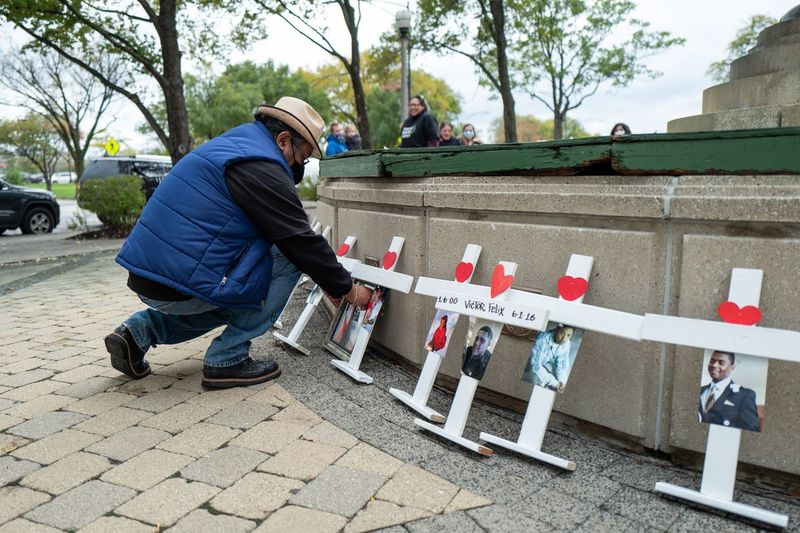 Salvadoras Aguado, kurio sūnus Alejandro buvo mirtinai nušautas 2019 m., spalio 30 d., šeštadienio popietę, klūpo prie kryžiaus su sūnaus nuotrauka per žmonių, kurių artimieji buvo nužudyti Čikagoje prie Kuko apygardos baudžiamojo teismo, Little Village kaimynystėje. , 2021. Renginį organizavo Teisingumo ieškančios šeimos ir tėvai už taiką ir teisingumą.