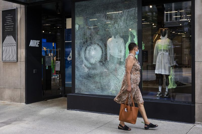 En kvinna går förbi Nike vid 669 N. Michigan Ave. på Magnificent Mile efter att plundring bröt ut över natten i Loop och omgivande kvarter, måndag morgon den 10 augusti 2020.