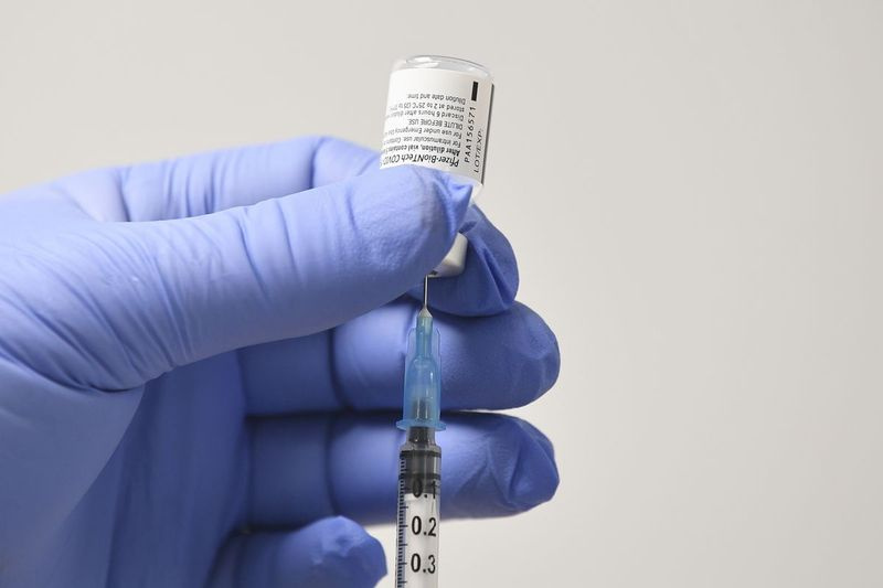 Zamestnanec používa ihlu a ampulku s vakcínou Pfizer-BioNTech Covid-19 na prípravu dávky v očkovacom zdravotnom stredisku v prvý deň najväčšieho imunizačného programu v histórii Spojeného kráľovstva 8. decembra 2020.