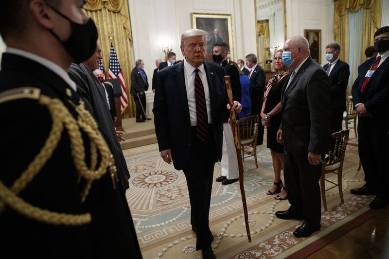 President Donald Trump bærer en spaserstokk gitt til ham av senator Lamar Alexander, R-Tenn., etter en lovsigneringsseremoni i Det hvite hus 4. august 2020,