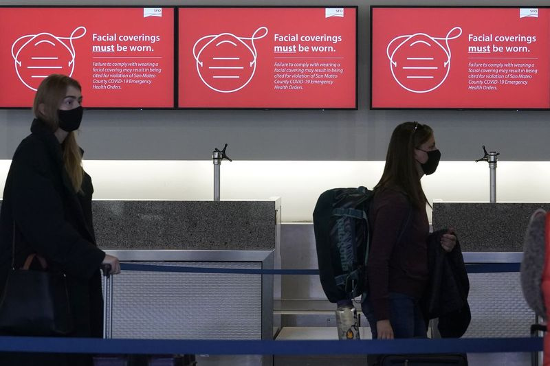 Σε αυτήν τη φωτογραφία αρχείου στις 22 Δεκεμβρίου 2020, εμφανίζονται πινακίδες που συμβουλεύουν τις απαιτήσεις κάλυψης του προσώπου καθώς οι ταξιδιώτες στέκονται στην ουρά σε ένα γραφείο της Delta Air Lines στο Διεθνές Αεροδρόμιο του Σαν Φρανσίσκο.