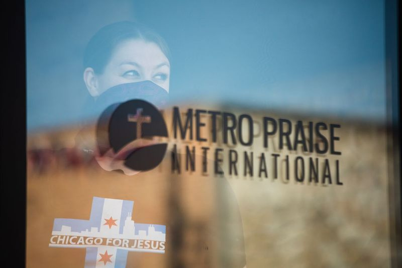 Člen Metro Praise International stojí u dveří kostela, protože bohoslužba se koná 24. května 2020. Kostel je jedním z kostelů v celém Chicagu, které se vzpírají nařízení guvernéra JB Pritzkera o úkrytu na místě, který omezuje v - bohoslužba do 10 osob. | Pat Nabong/Sun-Times