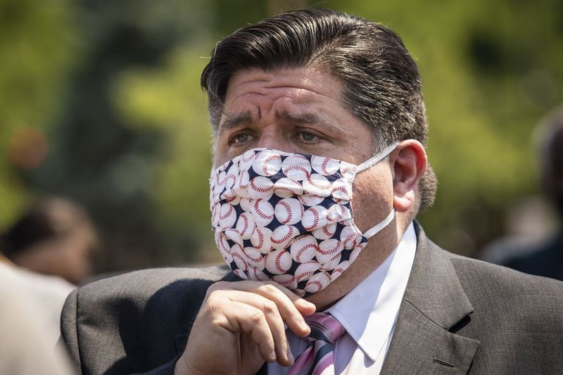 Gubernators J.B. Pritzker pielāgo savu sejas masku pēc preses konferences 2020. gada jūnijā.