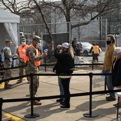 En medlem av Illinois National Guard kontrollerar en persons temperatur utanför covid-19 massvaccinationsplatsen som sattes upp på parkeringsplatsen vid United Center.