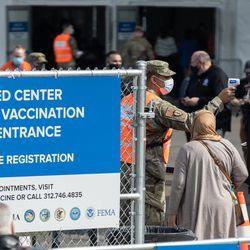 En medlem av Illinois National Guard kontrollerar en persons temperatur utanför massvaccinationsplatsen för covid-19 som sattes upp på parkeringsplatsen för United Center i Near West Side-området på öppningsdagen för den nya massvaccinationsplatsen, tisdag morgon 9 mars 2021.