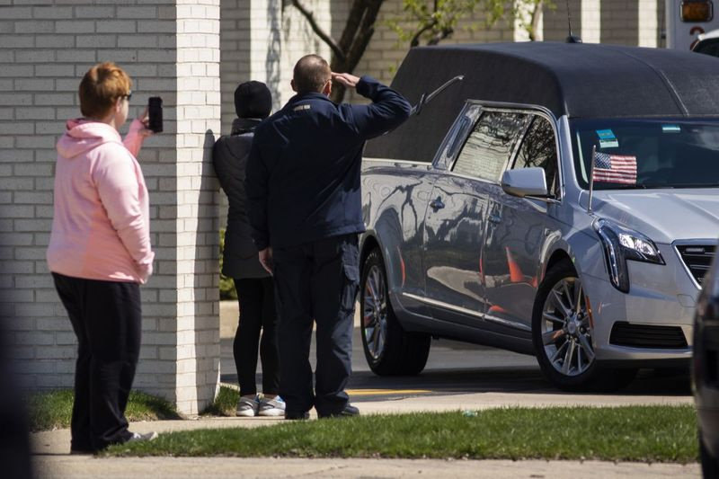 En mann hilser mens likbilen med Chicago-politibetjent Marco DiFranco forlater Cumberland Funeral Chapels i april 2020.