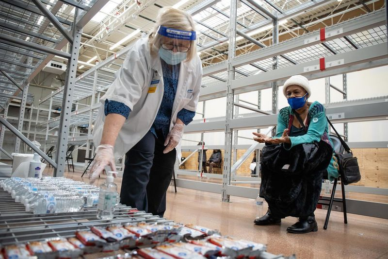 Gretchen Leider, gerente do centro de visão do Walmart, pega uma garrafa de água para Alice Collins enquanto ela está sob observação após receber a vacina Moderna COVID-19 no Walmart no bairro de Austin na terça-feira.
