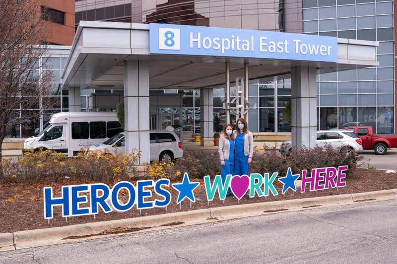 As enfermeiras de cuidados intensivos Kirsten Shea, RN (L) e Kathryn Lullo, RN (R) posam para um retrato em frente a placas que dizem que os heróis trabalham aqui, do lado de fora do AMITA Health Alexian Brothers Medical Center Elk Grove Village em dezembro de 2020.
