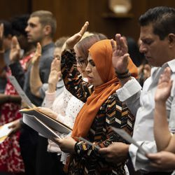 Jordanijoje gimusi 36 metų Sabra Isa (centre, oranžine spalva) yra viena iš 99 žmonių iš 33 šalių, prisiekusių ištikimybės priesaiką per natūralizacijos ceremoniją, kad užbaigtų tapimo JAV piliečiu procesą Dirkseno federaliniame rūmuose. Teismo rūmai, antradienis, 2019 m. liepos 2 d.