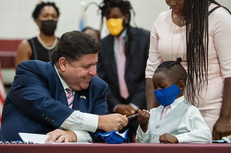 Guvernatorul J.B. Pritzker îi dă un stilou lui Jett Hawkins în timp ce semnează Actul Jett Hawkins la liceul comunitar Uplift din cartierul Uptown vineri.