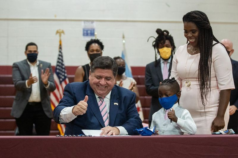 Guvernatorul J.B. Pritzker dă cu degetul mare în sus în timp ce semnează Actul Jett Hawkins alături de Jett Hawkins și de mama sa Ida Nelson, la Uplift Community High School din cartierul Uptown, vineri.