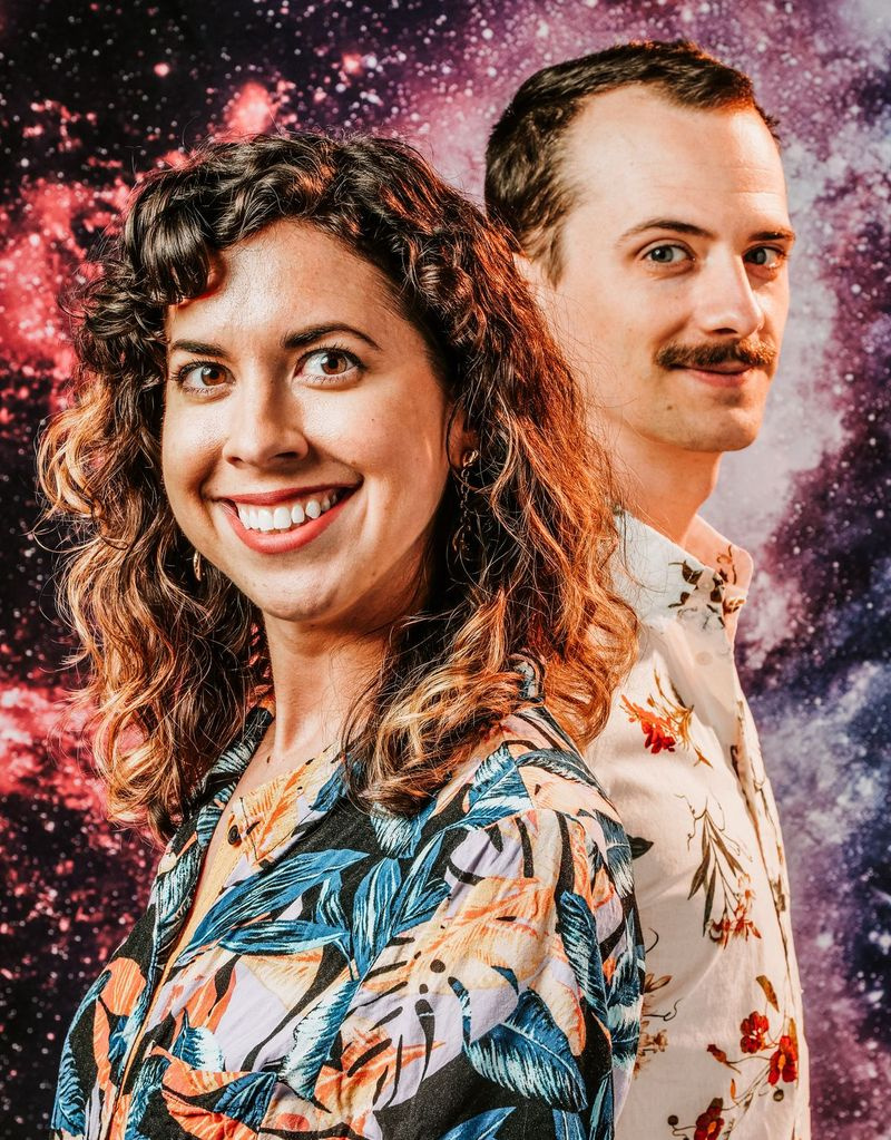 Prowadzący podcast REACH Meredith Stepien (po lewej) i Brian Holden (po prawej) pozują do zdjęcia promocyjnego.