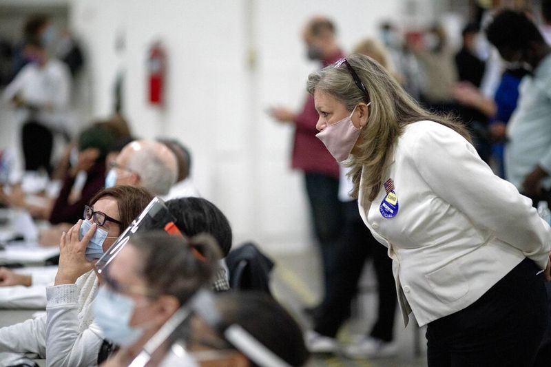 Contestatorul electoral republican de la dreapta veghează asupra inspectorilor electorali în timp ce examinează un buletin de vot în timp ce voturile sunt numărate până la primele ore ale dimineții la comisia centrală de numărare din Detroit.
