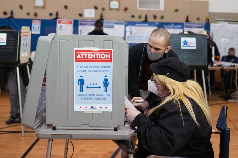 Lance Aguilar, de 31 años, trabajador electoral, ayuda a Dalinda Finch, de 63 años, a votar en Stone Scholastic Academy en el vecindario de West Rogers Park el martes 3 de noviembre de 2020 por la mañana.