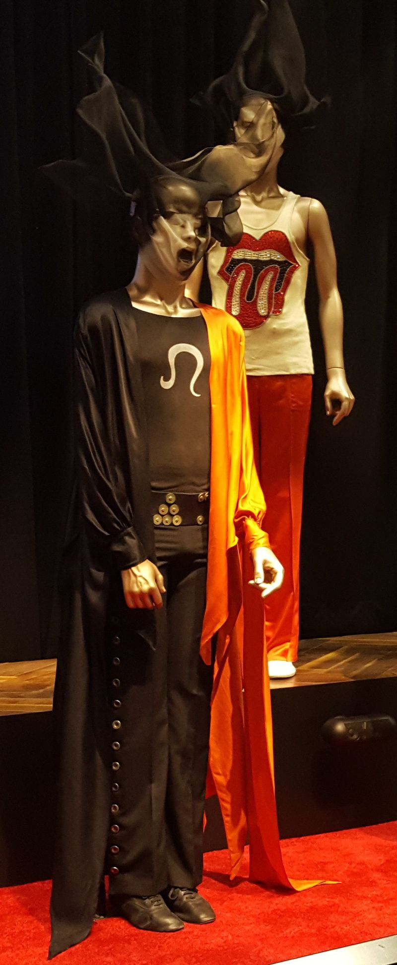 Das schwarz-rote Ensemble von Ossie Clark im Vordergrund mit Omega-T-Shirt und Umhang, getragen von Mick Jagger in Altamont und Madison Square Garden 1969. Charlie Watts kristallverziertes Hemd (Hintergrund), das während der US-Tour der Band 1972 getragen wurde. | MIRIAM DI NUNZIO PH
