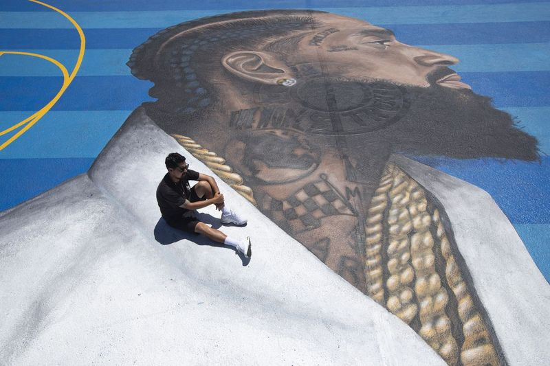 På det här fotot den 17 april 2019 poserar väggmålningskonstnären Gustavo Zermeno Jr. för bilder på en väggmålning för basketplan som han tillägnade den dödade rapparen Nipsey Hussle i Los Angeles. | AP Photo/Jae C. Hong