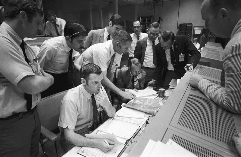 Sur cette photo du 15 avril 1970 mise à disposition par la NASA, un groupe de contrôleurs de vol se rassemble autour de la console de Glenn S. Lunney (au premier plan, assis), directeur de vol de Shift 4, dans la salle de contrôle des opérations de mission du Mission Control Center de Houston. Leur attention est attirée sur une carte météorologique du site d