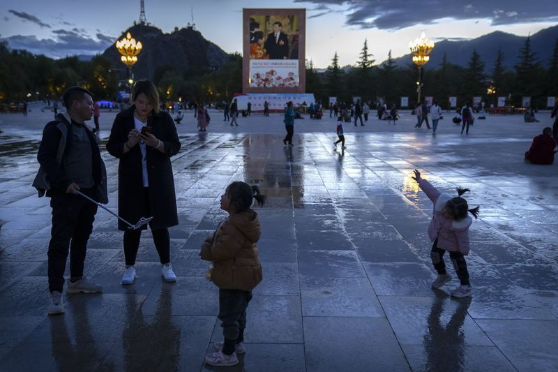 Turister står i nærheten av et stort veggmaleri som viser Kinas president Xi Jinping på et torg nær Potala-palasset i Lhasa i den vestlige Kinas autonome region Tibet.