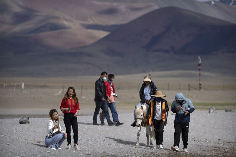 Turister går langs innsjøen og rir på en ponni i Namtso i den vestlige Kinas autonome region Tibet.