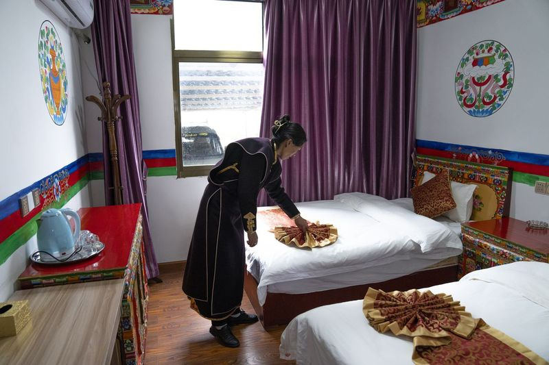 En kvinne i etnisk kjole tilpasser et sengeteppe ved sitt turisthjem i landsbyen Zhaxigang nær Nyingchi i det vestlige Kinas autonome region Tibet.