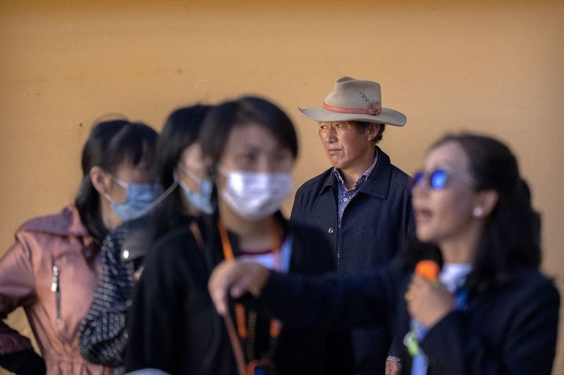 En tibetansk mann står på en gårdsplass mens en reiseleder holder et foredrag for turister ved Potala-palasset i Lhasa i den vestlige Kinas autonome region Tibet.
