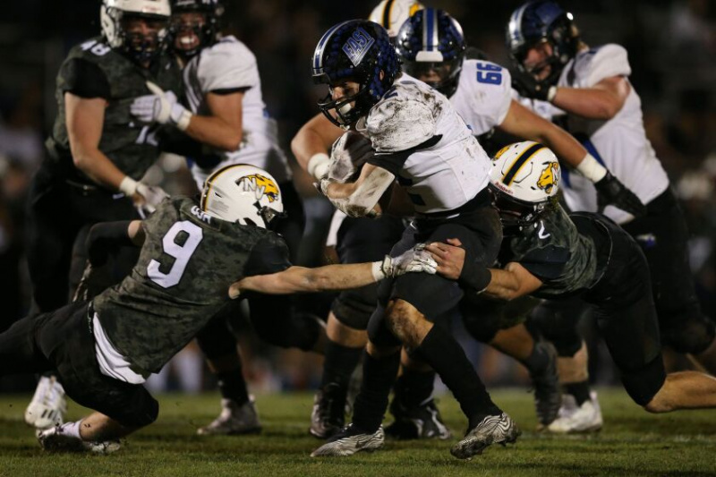   James Kwiecinski (2) da Lincoln-Way East protege a bola enquanto corre em linha reta, arrastando Cole Dutkovich (2) e Peyton Kuhl (9) de Neuqua Valley.