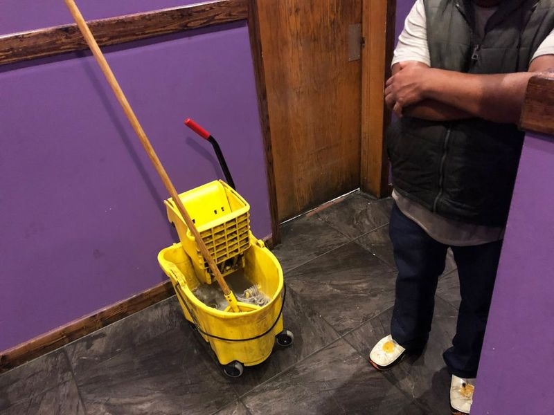 Een Latino-medewerker neemt even pauze van het dweilen van de vloer in een Chinees restaurant in Waukegan.