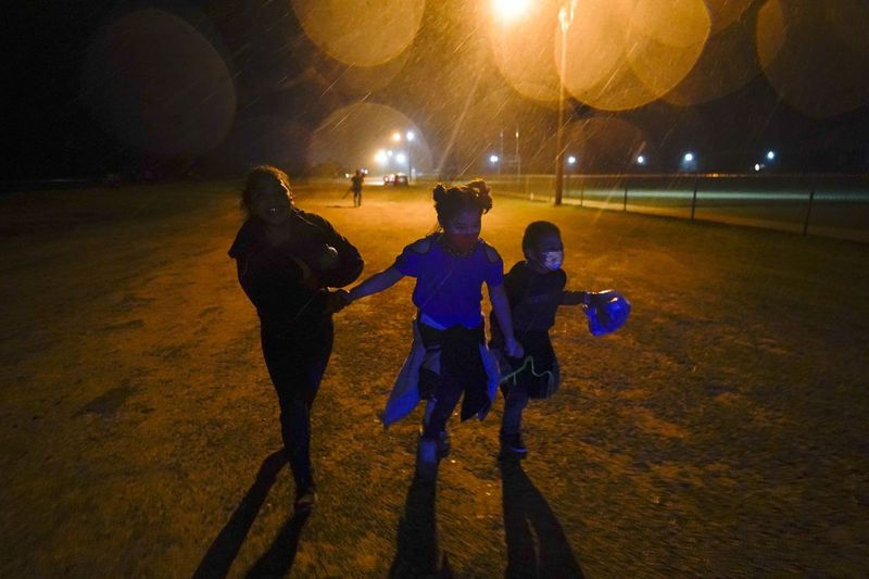 Drie jonge migrantenkinderen houden elkaars hand vast terwijl ze in de regen rennen naar een inlaatgebied nadat ze zichzelf hebben aangegeven bij het oversteken van de grens tussen de VS en Mexico in Roma, Texas.