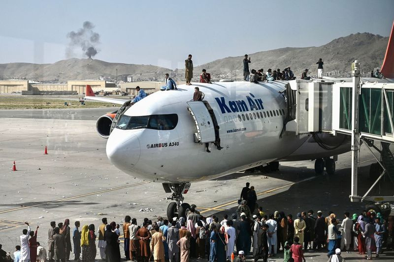 Afghanere klatrer op på toppen af ​​et fly, mens de venter i Kabul-lufthavnen mandag, efter en forbløffende hurtig afslutning på Afghanistans 20-årige krig, da tusindvis af mennesker mobbet byens lufthavn i forsøget på at flygte fra gruppens frygtede hårde islamistiske styre.