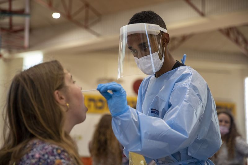 Antradienį Binjaminoje, Izraelyje, koronaviruso tyrimų centru virtusioje krepšinio aikštelėje medicinos darbuotojas tiria asmenį dėl COVID-19. Delta variantas dominuoja šioje grafystėje, kaip tikimasi per kelis mėnesius Ilinojaus valstijoje.