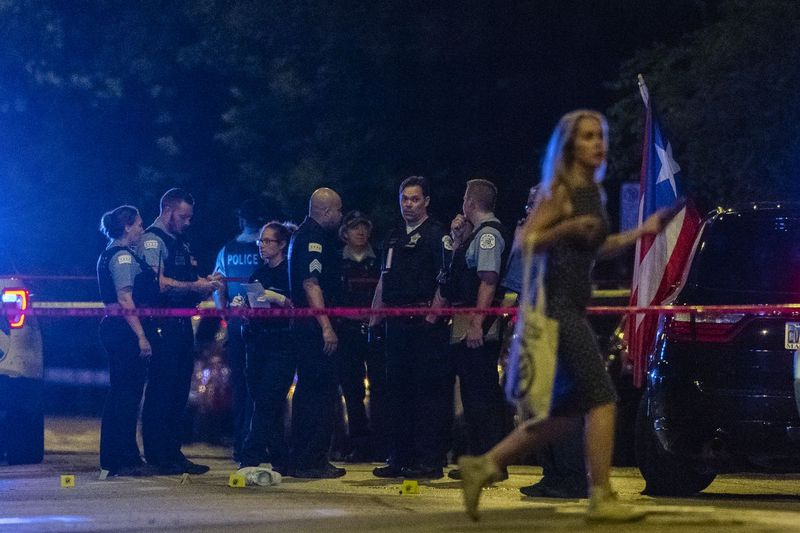 O femeie trece în timp ce poliția din Chicago lucrează la locul în care 2 persoane au fost împușcate, inclusiv un bărbat de 24 de ani care a fost împușcat și ucis, în strada 3200 West Division St. din cartierul Humboldt Park, sâmbătă, 19 iunie 2021.