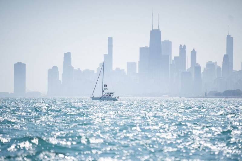   Łódź pływa po jeziorze Michigan w pobliżu Montrose Beach, podczas gdy widać panoramę Chicago.