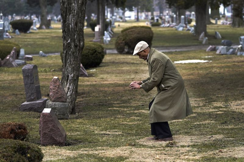 Tony Burroughs, PDG du Center for Black Genealogy de Chicago, se penche pour prendre une photo sur la tombe de ses arrière-grands-parents dans le cimetière d