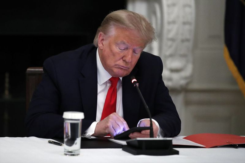 Na foto de arquivo desta quinta-feira, 18 de junho de 2020, o presidente Donald Trump olha para seu telefone durante uma mesa redonda com governadores sobre a reabertura de pequenas empresas da América, no State Dining Room da Casa Branca em Washington.