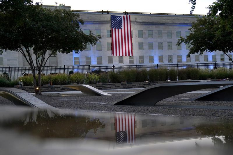 Un steag american este desfășurat la Pentagonul din Washington, sâmbătă, 11 septembrie 2021, la răsăritul soarelui, în dimineața celei de-a 20-a aniversări de la atacurile teroriste. Steagul american este drapat peste locul impactului de la Pentagon. În prim-plan, Memorialul Național al Pentagonului 9/11, deschis în 2008, lângă situl, comemorează viețile pierdute la Pentagon și la bordul zborului 77 al American Airlines.