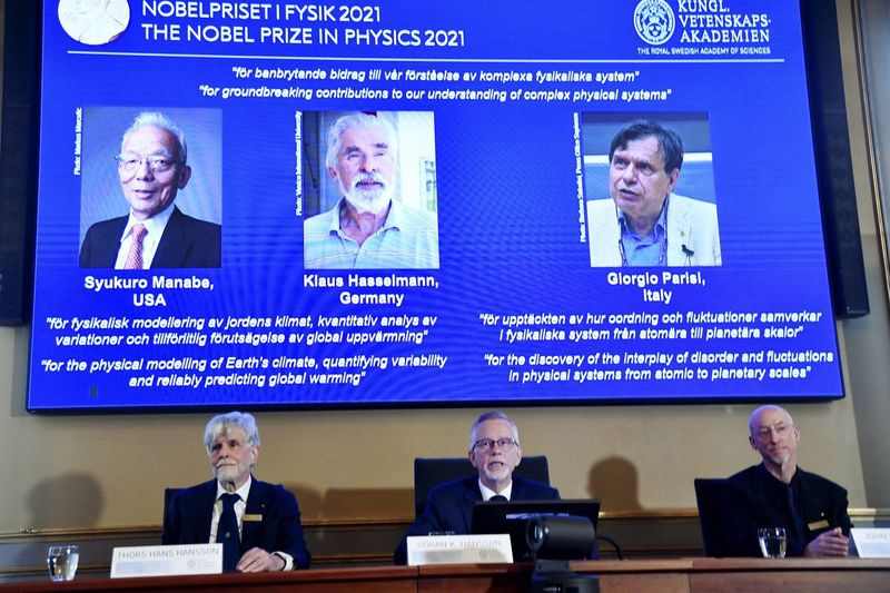 Generální tajemník Královské švédské akademie věd Goran Hansson, uprostřed, vlevo lemovaný členem Nobelova výboru pro fyziku Thorsem Hansem Hanssonem, vlevo a členem Nobelova výboru pro fyziku Johnem Wettlauferem, vpravo, oznamuje vítěze 2021 Nobelova cena za fyziku na Královské švédské akademii věd ve Stockholmu, Švédsko, úterý 5. října 2021.