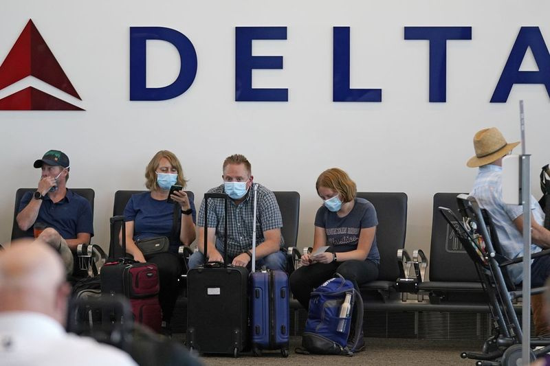Folk sidder under Delta-skiltet i Salt Lake City International Airport den 1. juli 2021 i Salt Lake City. Delta Air Lines vil ikke tvinge ansatte til at blive vaccineret, men det vil få uvaccinerede arbejdere til at betale en månedlig afgift på $200. Delta sagde onsdag den 25. august 2021, at det også vil kræve ugentlige tests for uvaccinerede medarbejdere fra næste måned, selvom flyselskabet siger, at det vil betale omkostningerne ved den test.