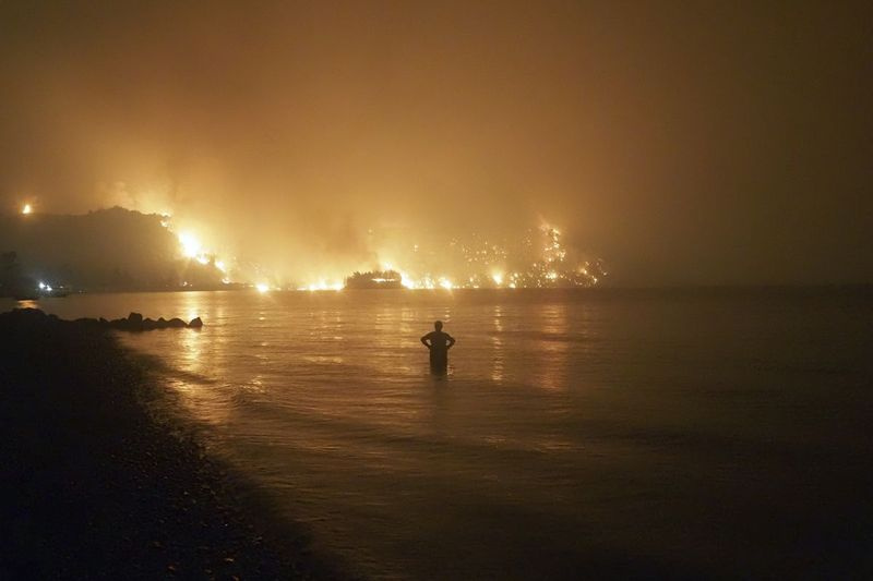 Na této souborové fotografii z pátku 6. srpna 2021 muž sleduje, jak se lesní požáry blíží k pláži Kochyli poblíž vesnice Limni na ostrově Evia, asi 160 kilometrů (100 mil) severně od Atén v Řecku.
