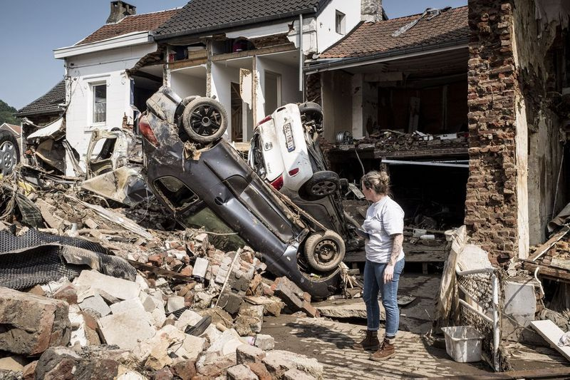 Na této souborové fotografii z pondělí 19. července 2021 se žena dívá na auta a domy poškozené po přívalovém dešti způsobeném záplavami v belgickém Lutychu.