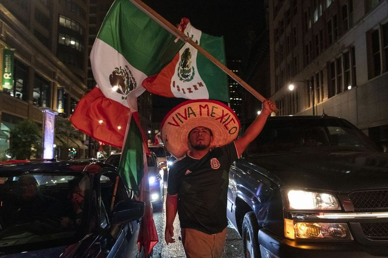 昨年のメキシコ独立記念日のためにシカゴのダウンタウンで何百人もの人々が祝うとき、男性がIda B. WellsDr。にメキシコの旗を掲げて車の間を歩きます。