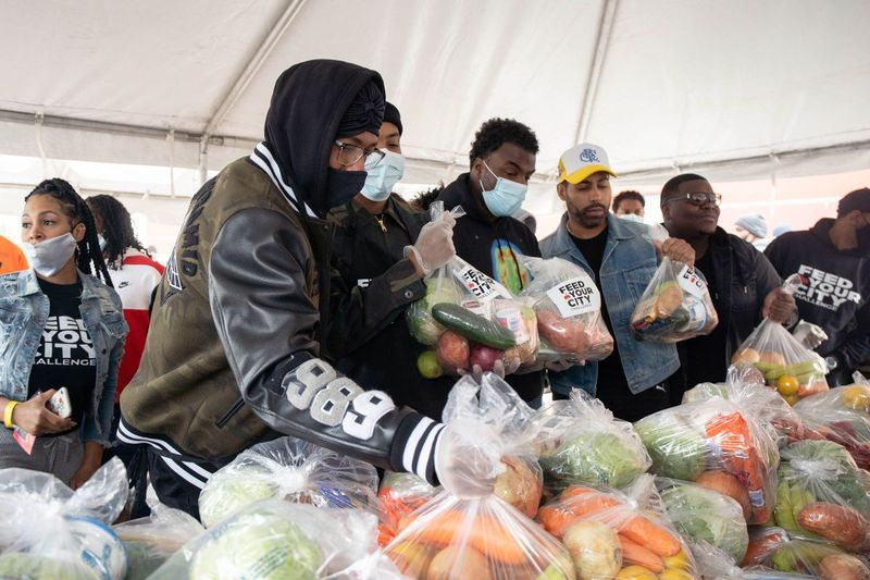 Komik a rapper Nick Cannon (vlevo) a rapper G Herbo (vpravo) drží tašky s jídlem v sobotu během akce Feed Your City Challenge, food drive, kterou založil zakladatel Suave House Records Tony Draper a bývalý hráč NBA Ricky Davis na parkovišti u Pullman Community Center.