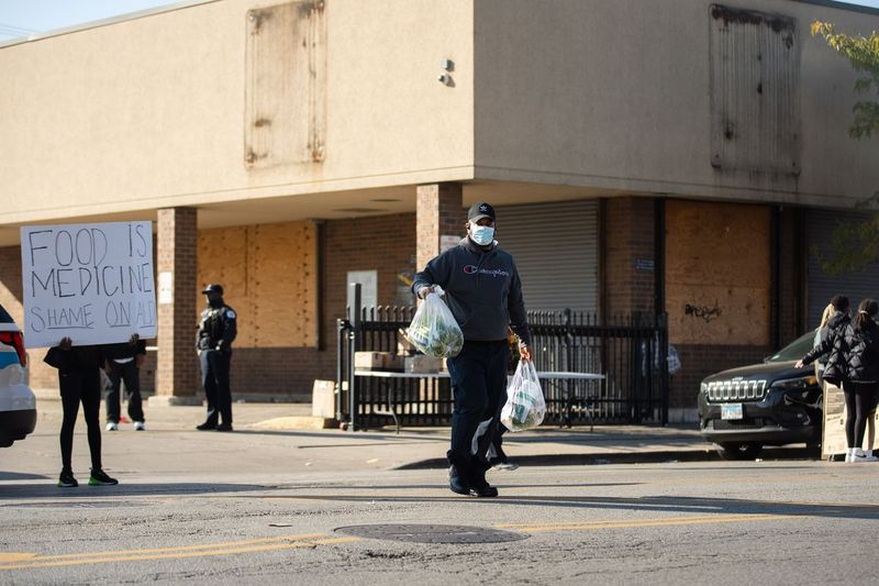 Jesus Ramirez überquert die Straße, während er während einer Lebensmittelverteilungsveranstaltung vor dem geschlossenen Aldi in 3835 W. Madison St. im Stadtteil West Garfield Park am Samstagmorgen, 6. November 2021, zwei Tüten mit Lebensmitteln in der Hand hält.