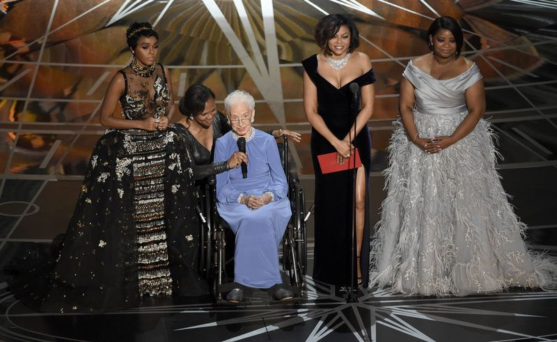 Janelle Monae (kairėje), Taraji P. Hensonas (antra dešinėje), kuri ją vaidino filme, ir Octavia Spencer (dešinėje), pristato sėdinčią Katherine Johnson, kuri yra filmo „Paslėptos figūros“ įkvėpėja, įteikiant apdovanojimą už geriausią dokumentinį filmą „Oskarai“ 2017 m. vasario 26 d.