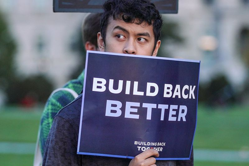 Un tânăr ține un semn în sprijinul proiectului de lege Build Back Better la un miting din 18 noiembrie 2021, cu o zi înainte ca Parlamentul să adopte legislația.
