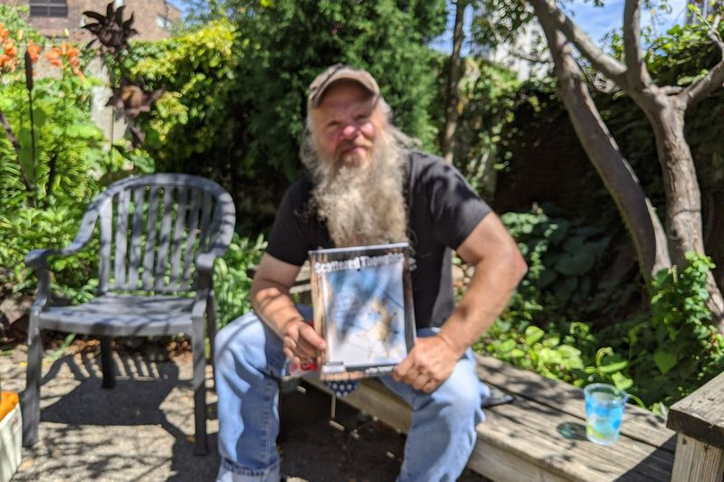 Tim Spike Davis pozuje ze swoją niedawno wydaną książką kreskówek, Scattered Thoughts, podczas wywiadu w przyulicznym ogrodzie w Uptown. Źródło: Dale Bowman